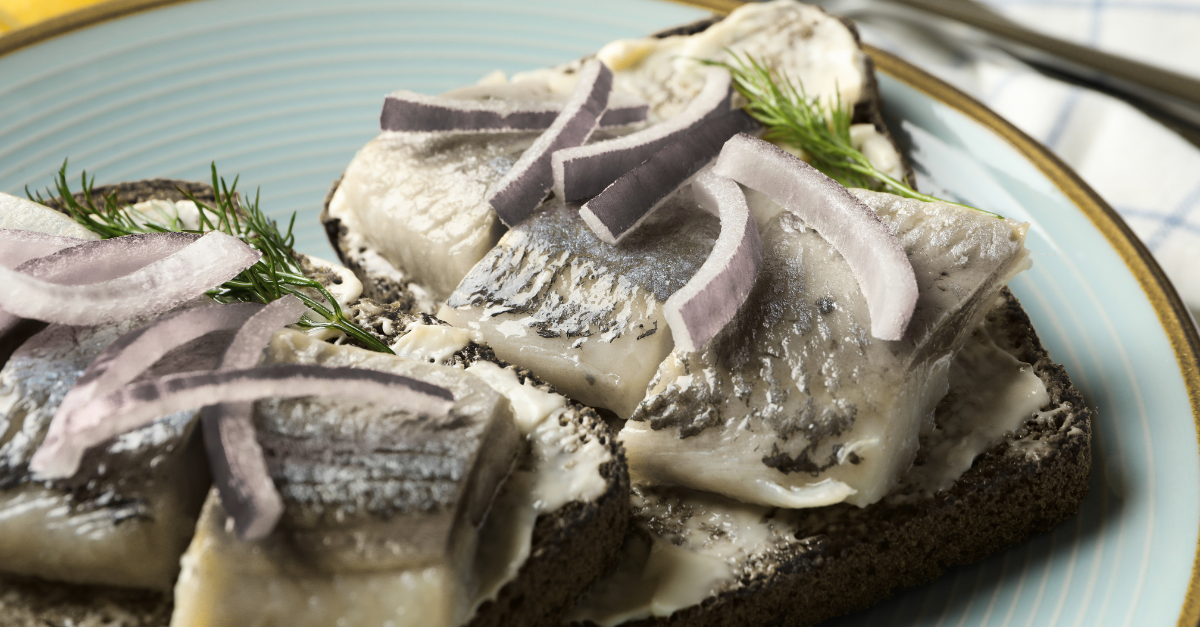 Sillbitar på en smörgås ligger på en tallrik.